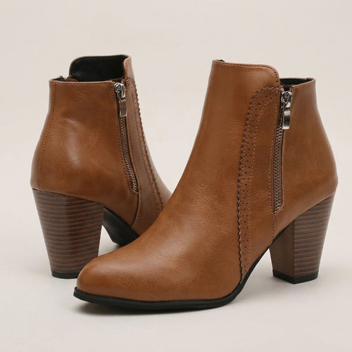 A pair of women's ankle boots in tan faux leather, featuring a stacked block heel, side zippers, and decorative stitching on the outer side, shown against a light beige background.