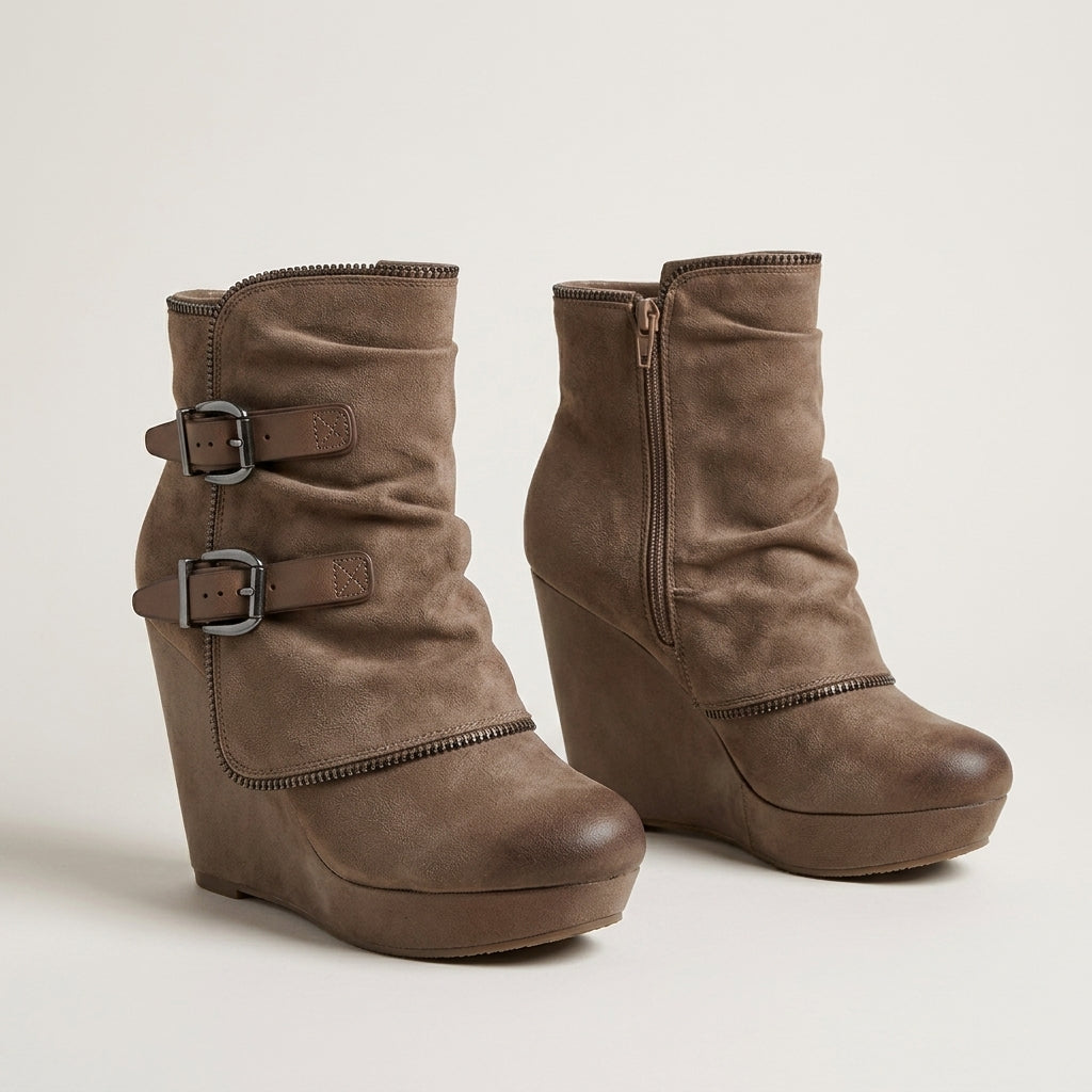 A pair of taupe brown suede wedge ankle boots with double buckle straps on one boot and a side zipper on the other, shown against a plain light beige background.